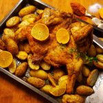 Oven-baked orange baked chicken with potatoes on a baking tray