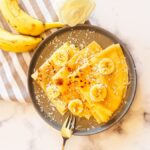 An overhead picture of crepes, garnished with some sliced banana.