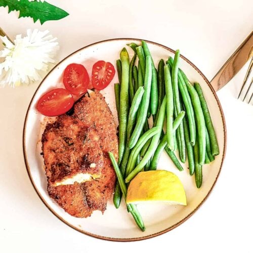 air fried tilapia on a plate, served with some green beans, cherry tomatoes, and a slice of lemon on the side.