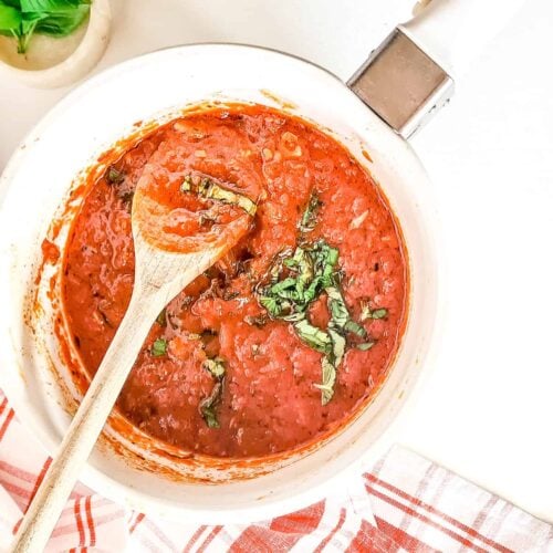 A picture of marinara in a non-metallic pot, garnished with some basil leaves.