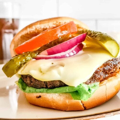 An air fryer hamburger topped with sliced vegetables and served on buns.