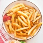 A plate of chips (also known as french fries), with some ketchup on the side.