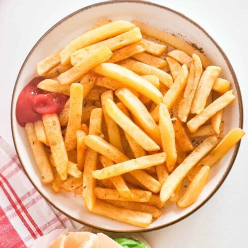 A plate of chips (also known as french fries), with some ketchup on the side.