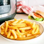 A picture showing a plate of chips and a Ninja Foodi Air Fyer with a hamburger in the background.