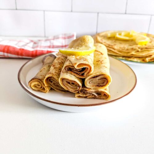 A side picture showing South African pancakes on a plate, garnished with some lemon on top.
