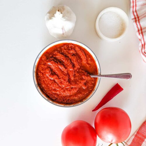 A picture showing African pili pili sauce, some tomatoes, garlic, and African bird eye chili.