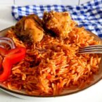 A picture showing a plate of Jollof rice with some fried chicken.