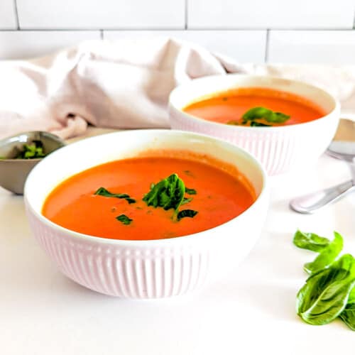 Homemade tomato soup in bowls, garnished with basil.