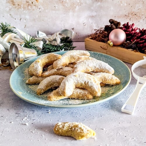 A plate of Vanillekipferl cookies with some Christmas decoration in the background.