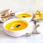 Bowls of pumpkin soup with slices of bread in the background.
