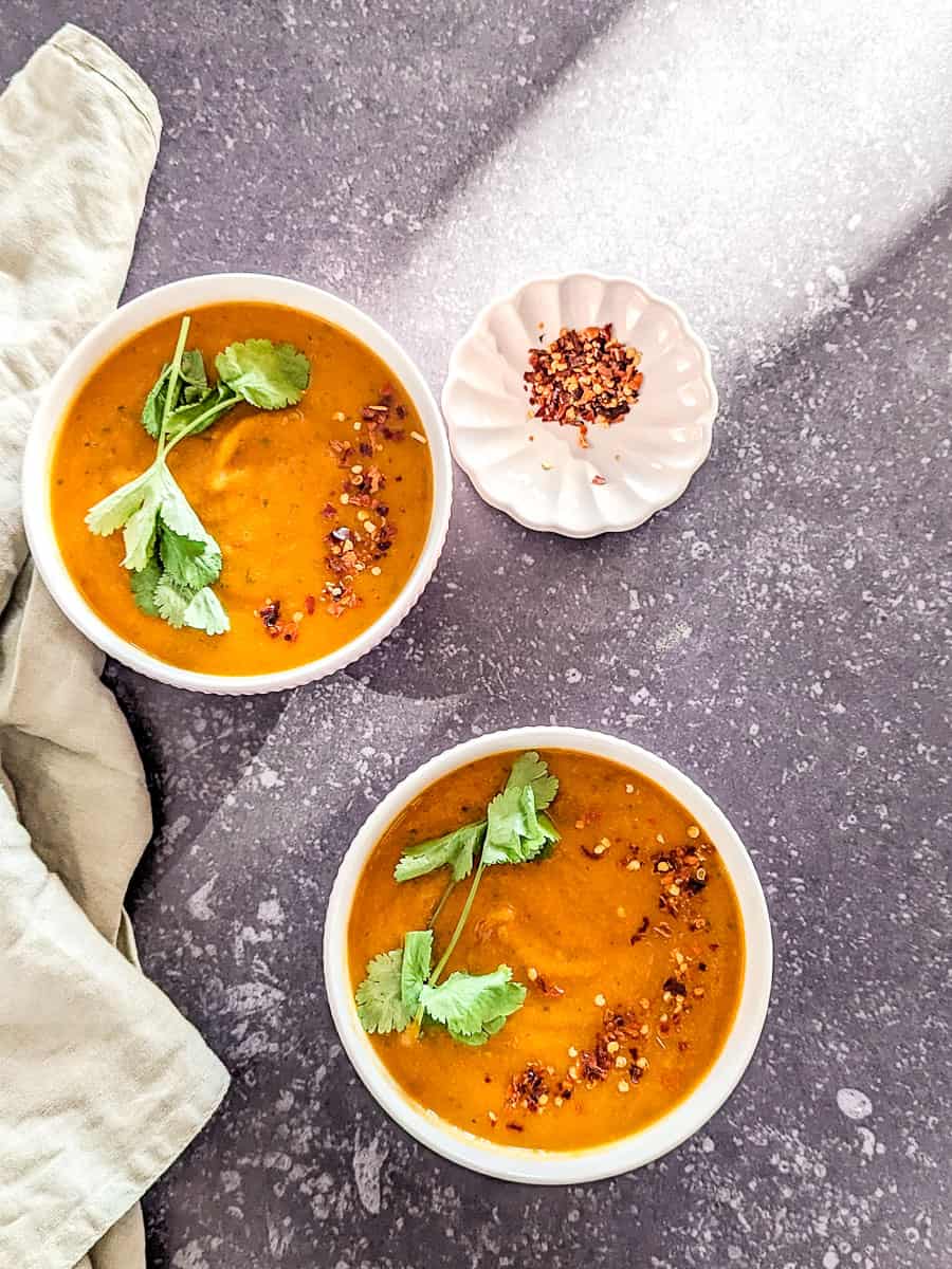 Two bowls of carrot soup on a black background.