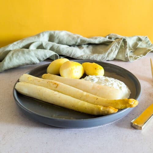 A plate of white asparagus with potatoes, and a yogurt dip.