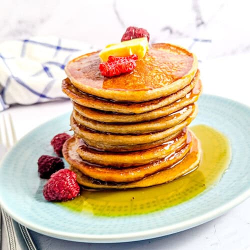 A stack of cottage cheese pancakes topped with berries, and maple syrup.