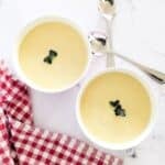 Two bowls of parsnip soup, garnished with some parsley leaves.