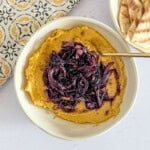 Hummus topped with balsamic onions in a small bowl.