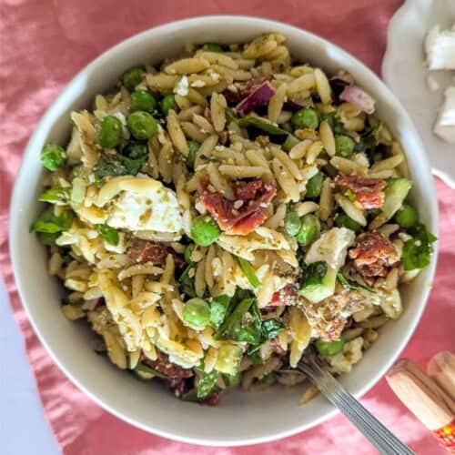 A square zoomed in image of orzo salad with feta, cucumber and peas in a bowl.