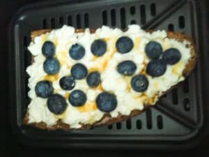 Bread topped with cottage cheese, blueberries and honey inside an air fryer basket.