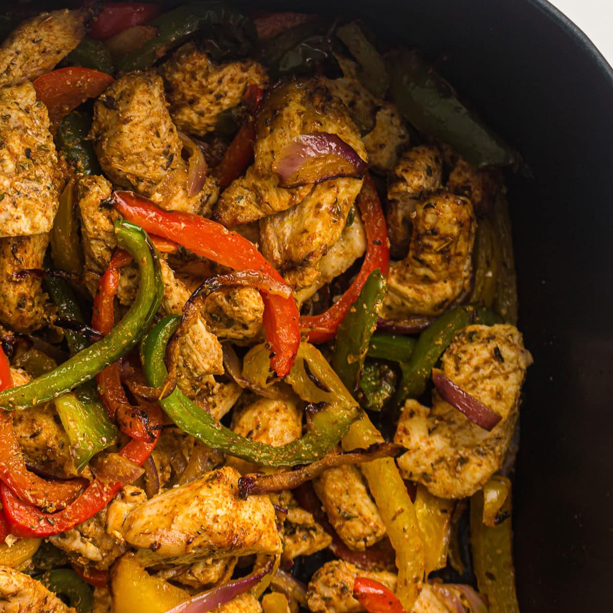 Air fried chicken fajita with bell peppers and onion cooked in an air fryer basket.