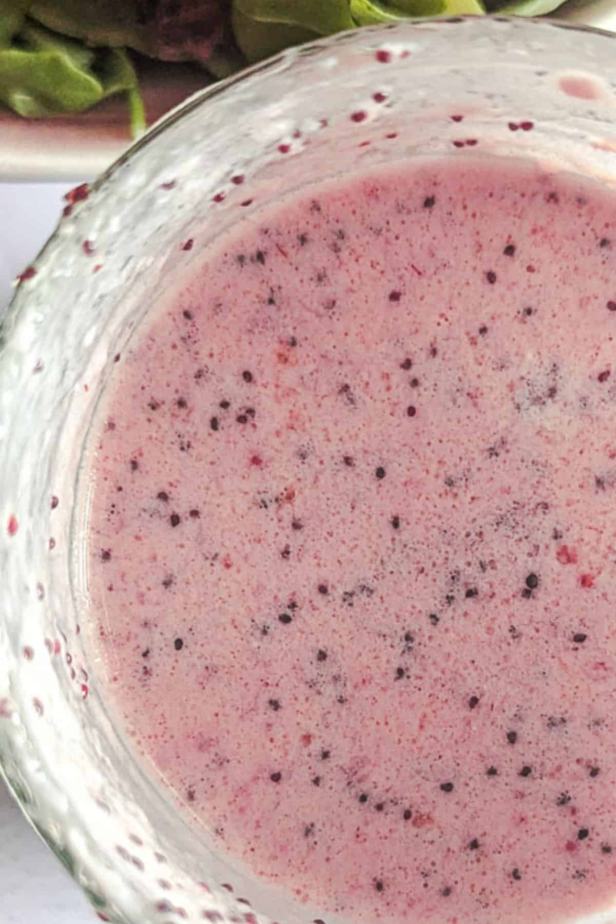 A glass of strawberry dressing with a salad in the background.