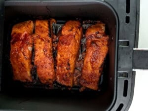 Cooked salmon fillets in an air fryer basket.