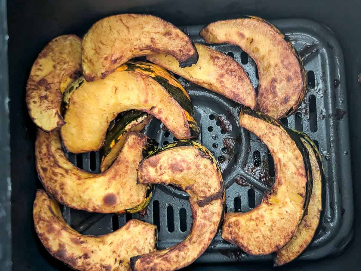 Air fryer basket with cooked acorn squash slices.