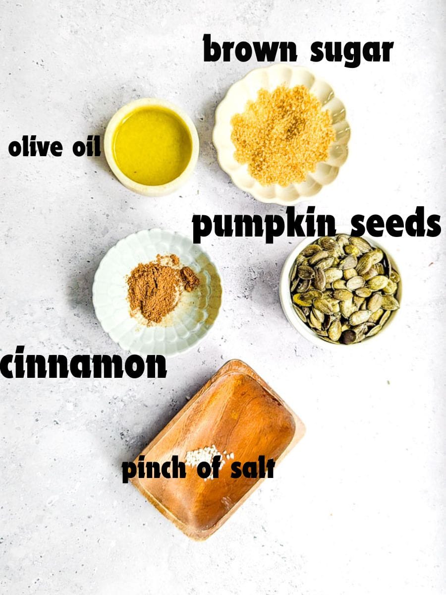 Bowls with olive oil, brown sugar, pumpkin seeds, ground cinnamon, and a pinch of salt arranged on a light surface.