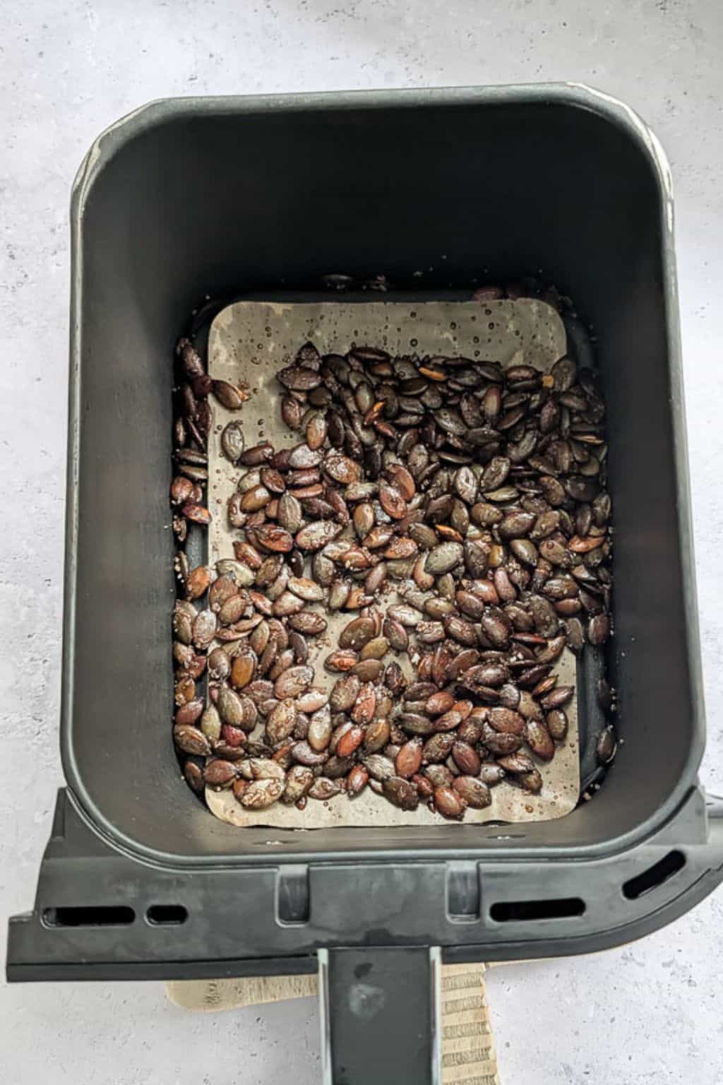 Roasted pumpkin seeds inside an air fryer basket.