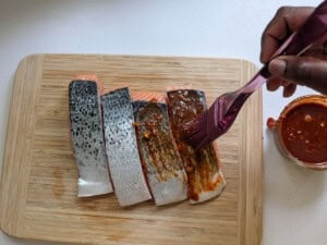 A person basting a uncooked salmon fillet with a spoonful of sauce.