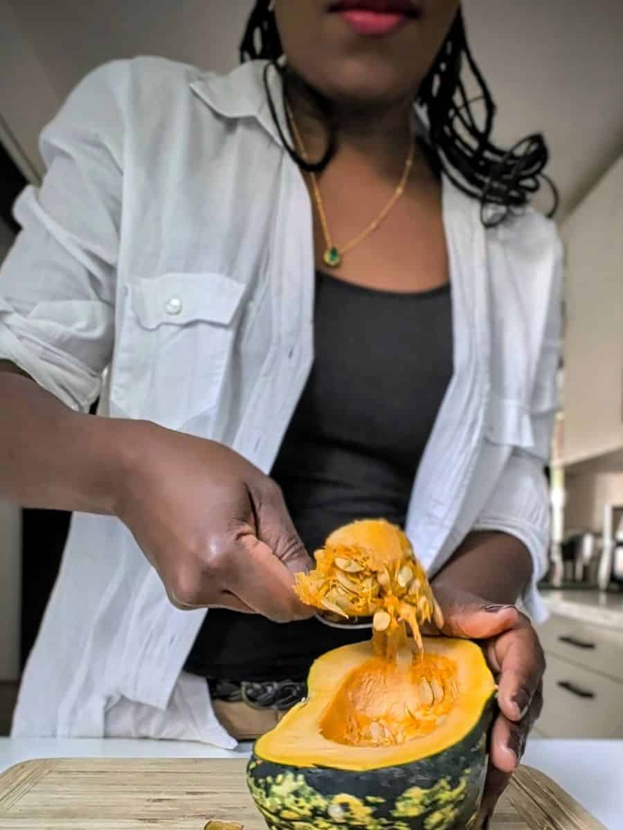 Scooping seeds from a halved squash in a kitchen.