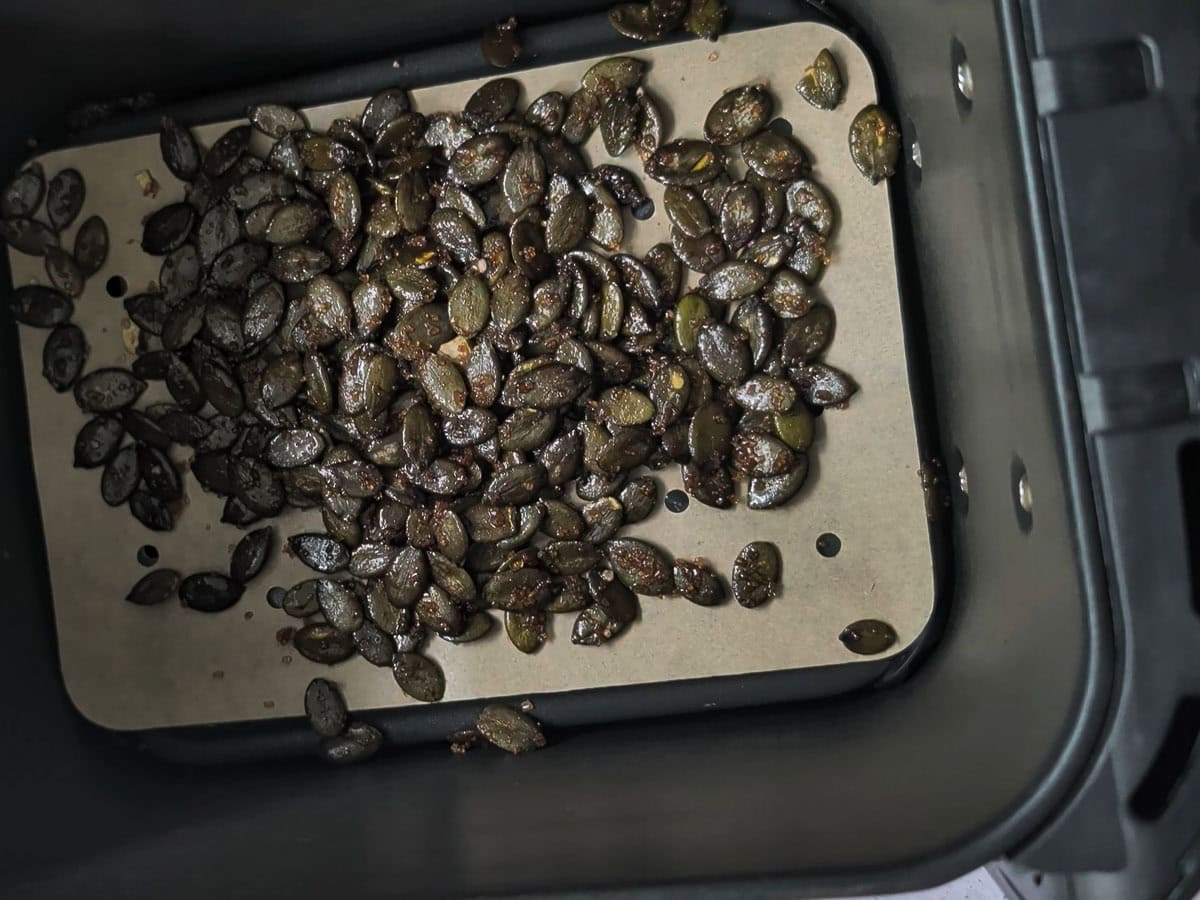 Pumpkin seeds spread in an air fryer basket on a liner.