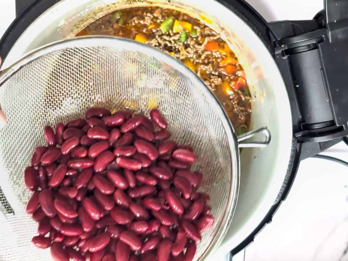Adding kidney beans to a pot of cooking chili.