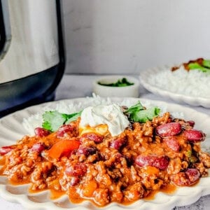 Chili con carne served on a plate with rice and sour cream, garnished with coriander leaves.