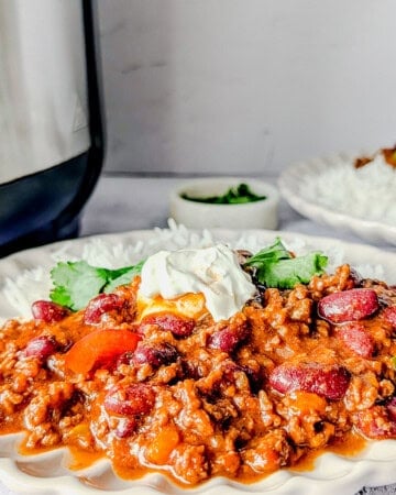 Chili con carne served on a plate with rice and sour cream, garnished with coriander leaves.
