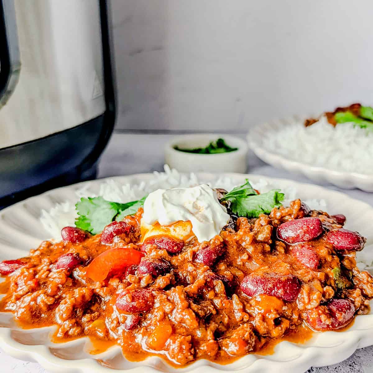 Chili con carne served on a plate with rice and sour cream, garnished with coriander leaves.