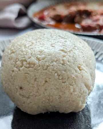 Oat flour fufu on a plate with some stew in the background.
