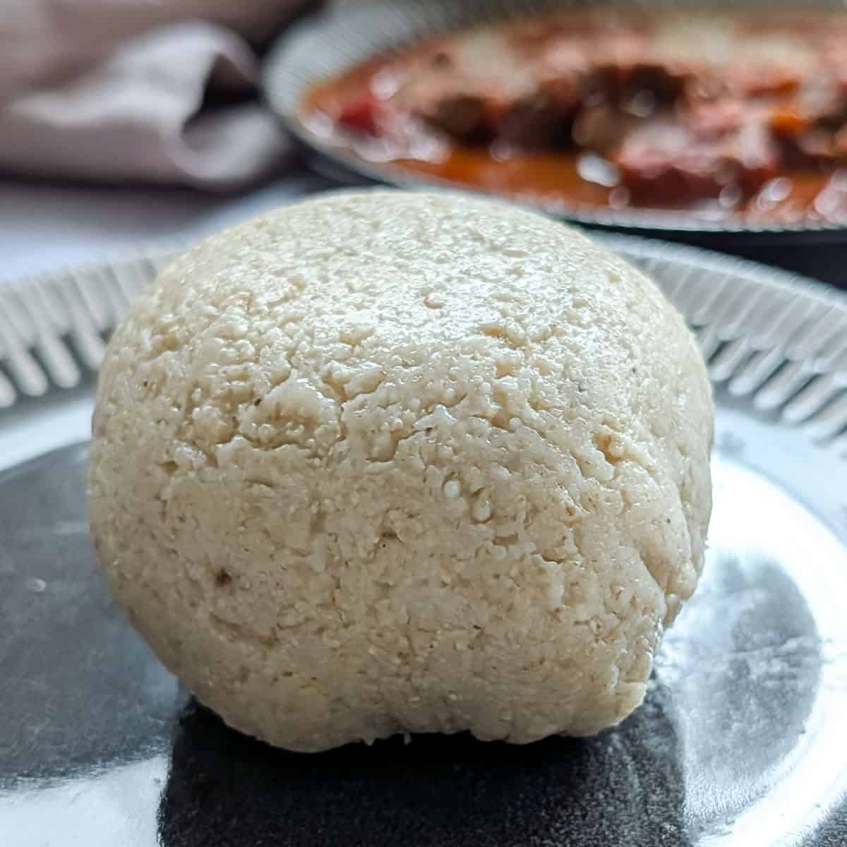 Oat flour fufu on a plate with some stew in the background.
