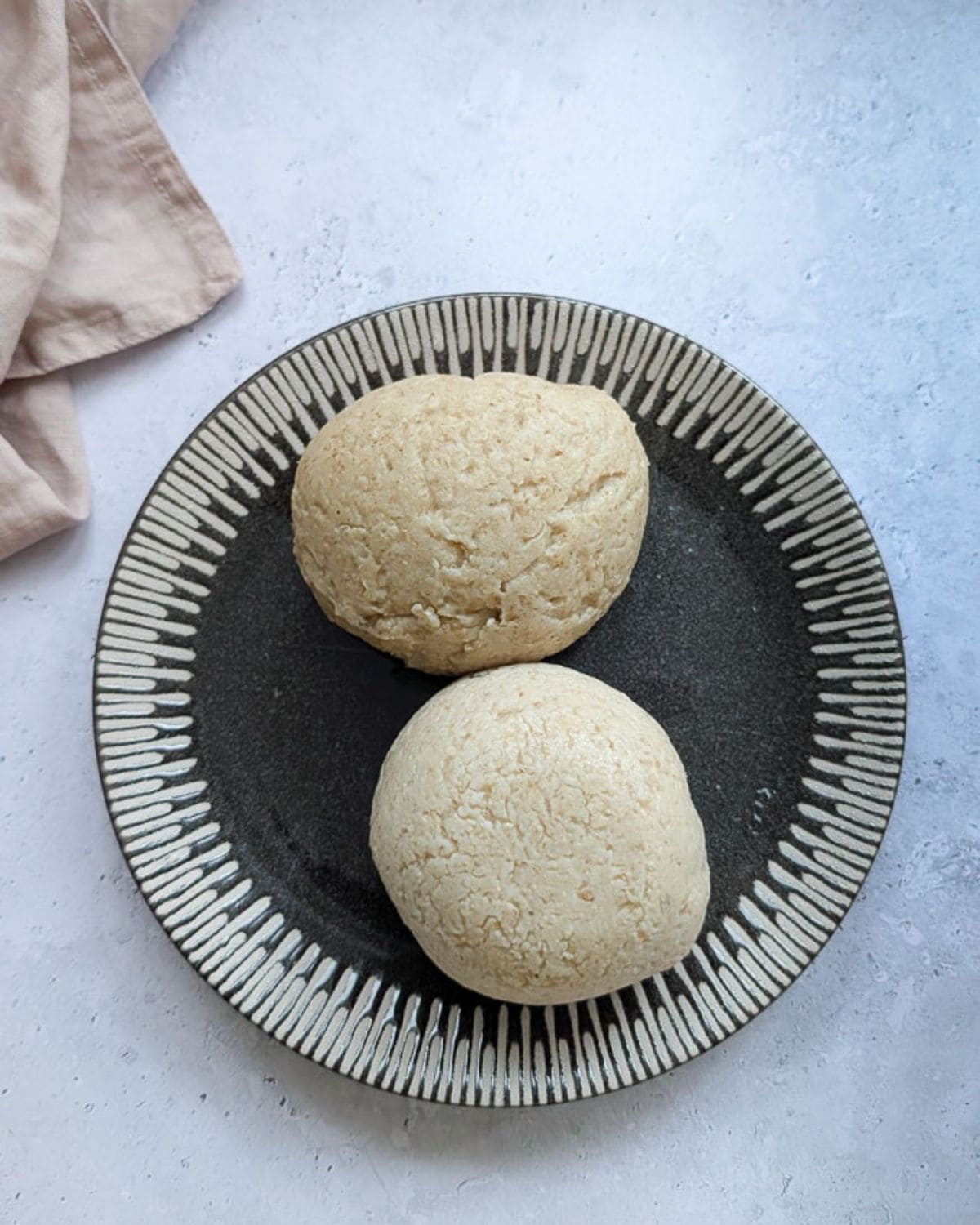 Two scoops of oat fufu served on a dark African-patterned plate.