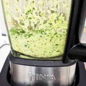 A close-up image of the Yassa chicken marinade ingredients blended into a smooth green mixture in a Ninja blender.