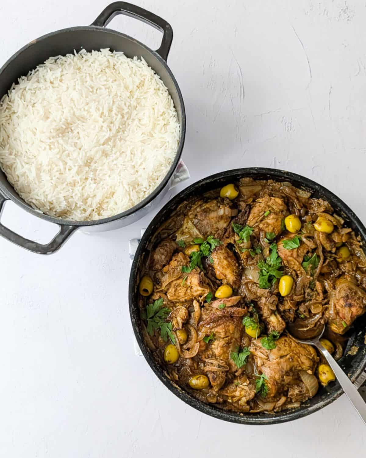 Yassa chicken in a pan next to a pot of cooked basmati rice.