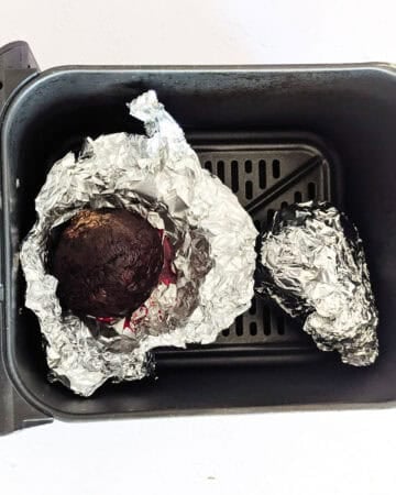 Whole roasted beets wrapped in foil inside an air fryer.