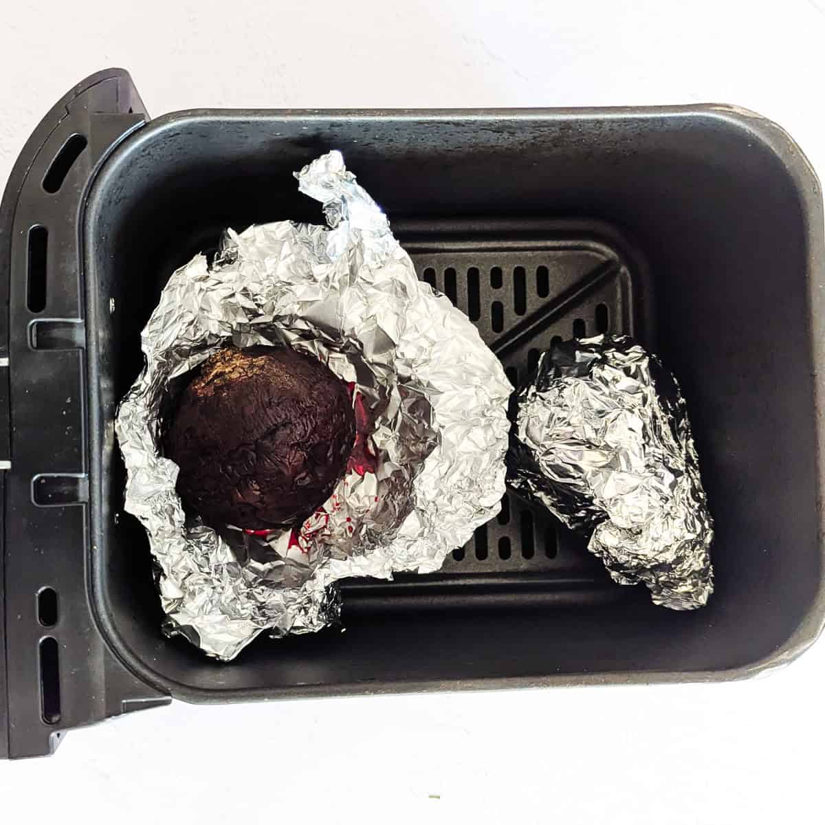 Whole roasted beets wrapped in foil inside an air fryer.