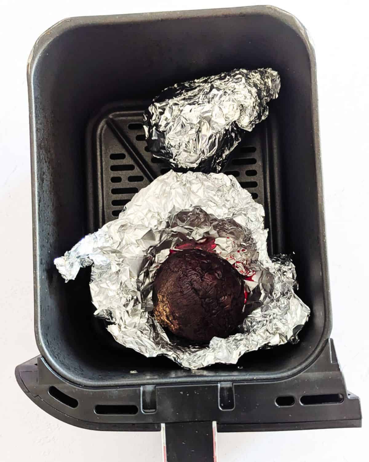 Air fryer basket with foil wrapped whole beets.