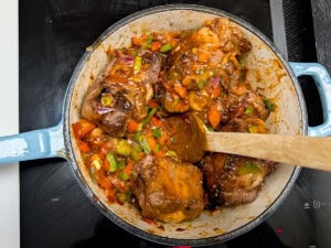 Oxtail pieces seared and cooking with onions, garlic, and bell peppers.