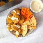 Air fryer frozen falafel on a plate with carrot sticks, pita bread, and tahini sauce.