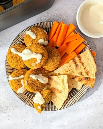 Air fryer frozen falafel on a plate with carrot sticks, pita bread, and tahini sauce.