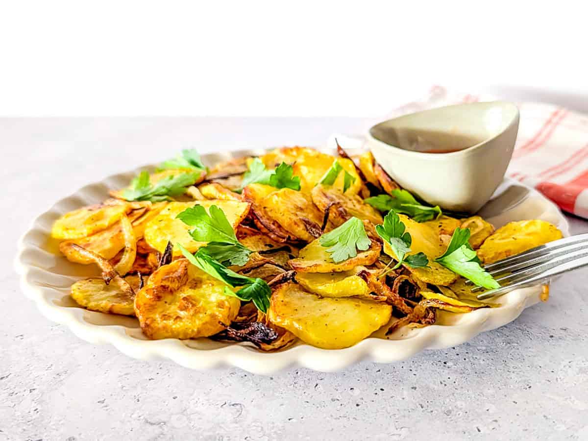A horizontal picture of air fryer sliced potatoes and onions served on a plate.