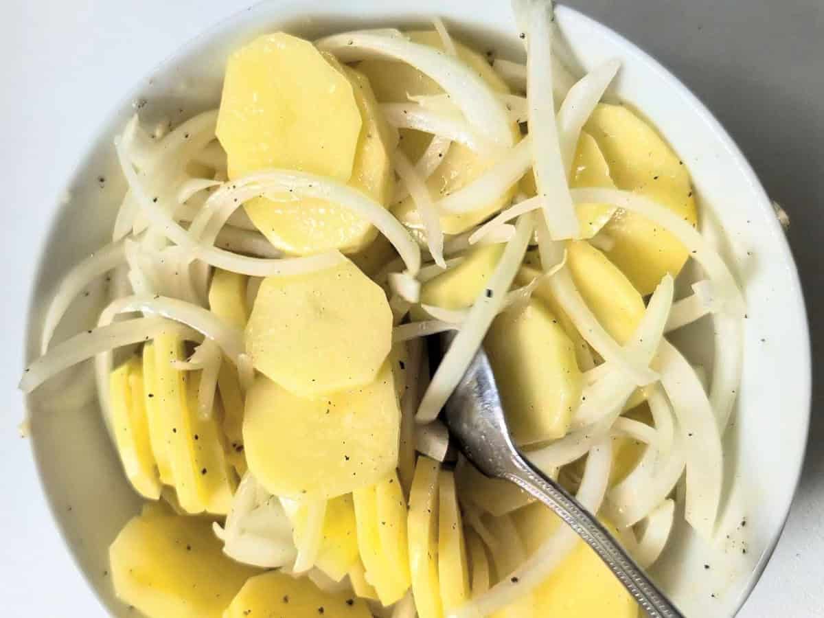 Sliced potatoes and onions coated in seasoning in a mixing bowl before air frying.