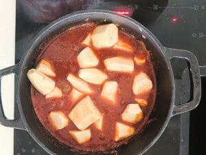 Green banana chunks added to a pot with a tomato-based sauce.