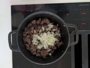 Diced onion added to browned beef in a pot.