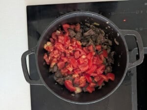 Diced tomatoes added to browned beef and onions in a pot.